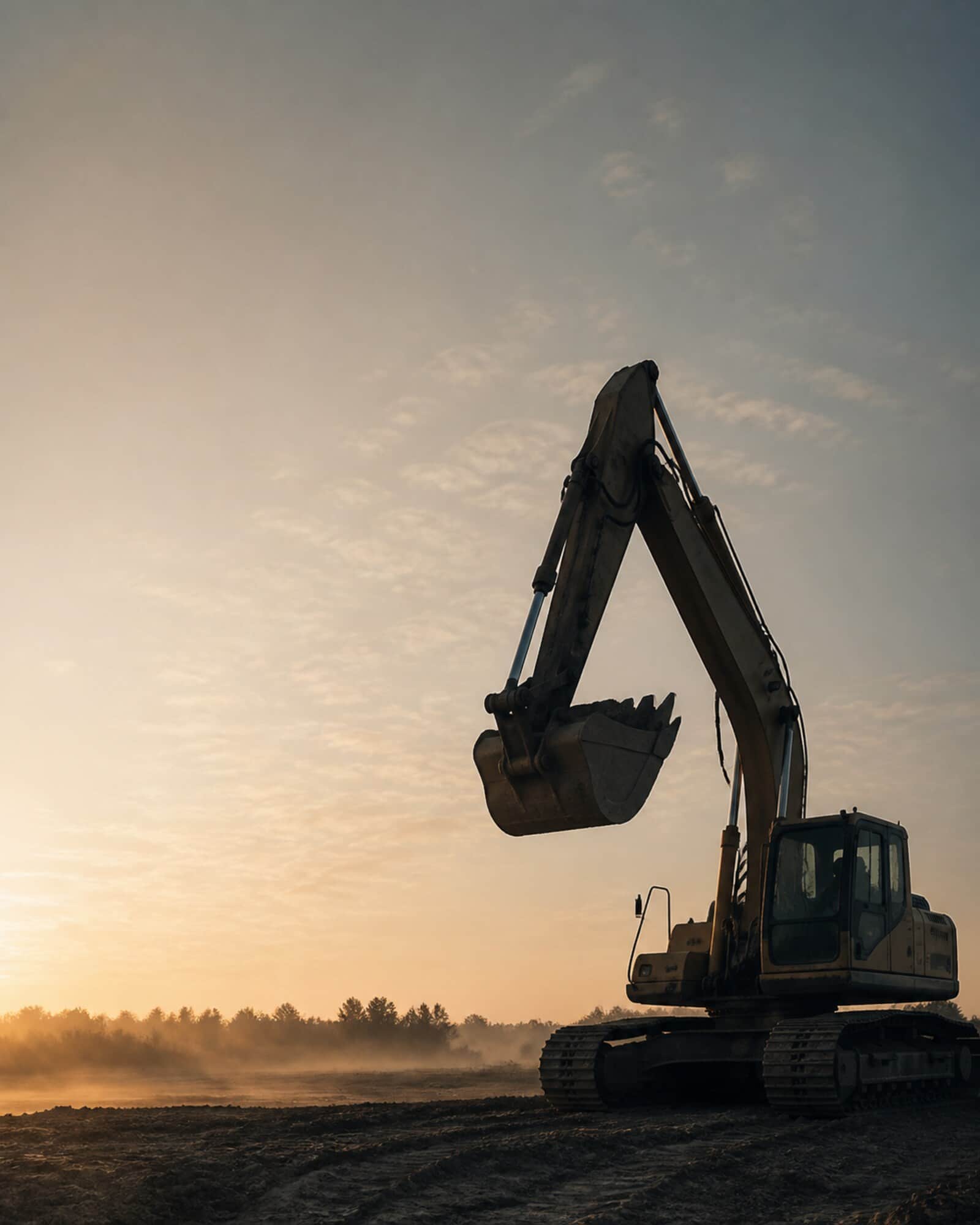 Excavator boom raised against a dawn sky on a graded earth site