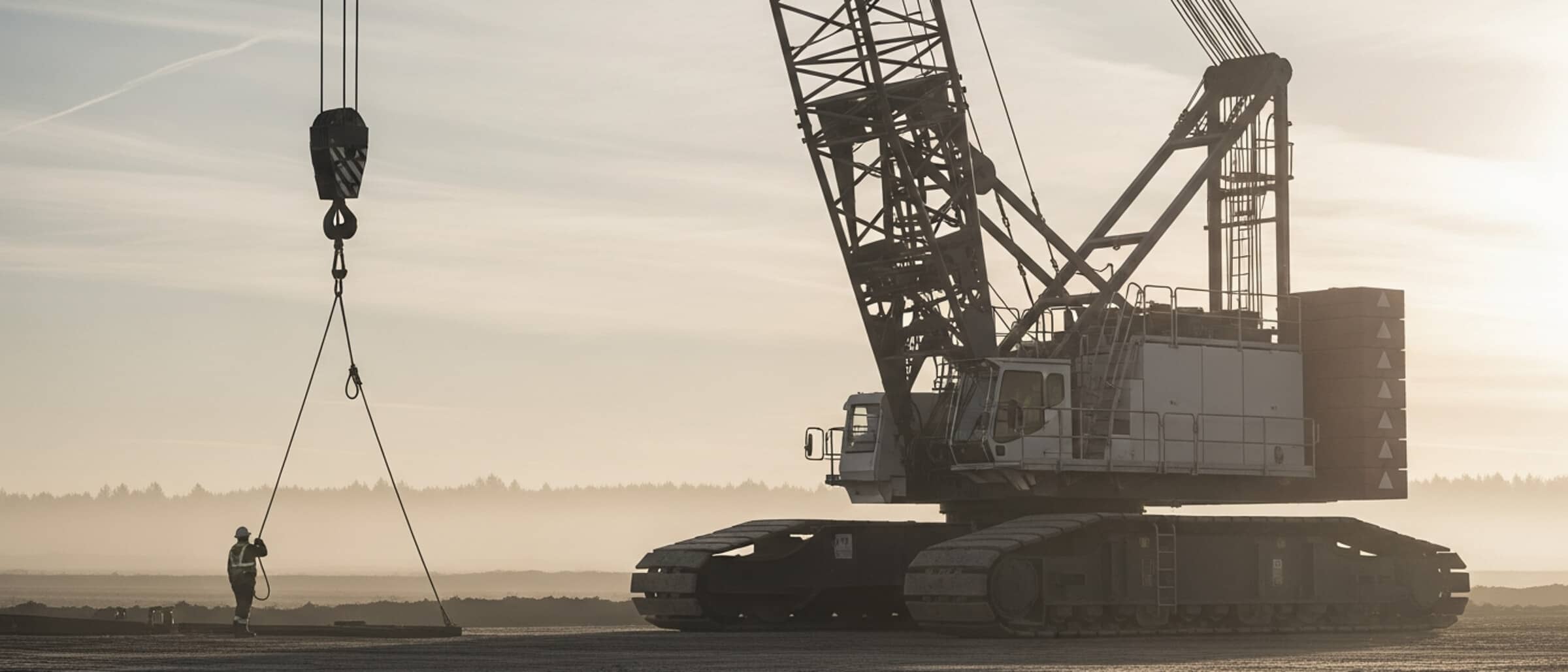 Crawler crane counterweights with a distant worker for scale at dawn